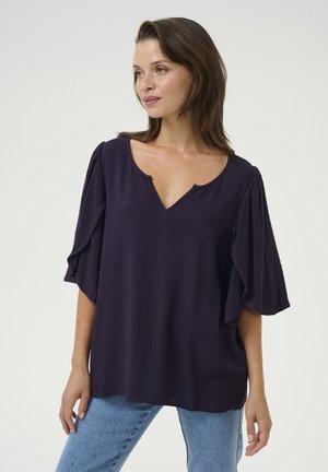 Dark purple blouse featuring a V-neck, short flutter sleeves, and a textured pattern. Paired with light blue denim jeans.
