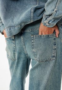 Vaaleansiniset farkut, joissa on rento istuvuus, taka-taskut ja näkyvät ompelusarjat. Kankaan pinta on kuluneen näköinen.