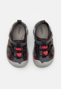 Šedé vodní boty s gumovou podrážkou, černými a červenými akcenty, nastavitelné tkaničky a otevřené části pro prodyšnost a odvod vody.