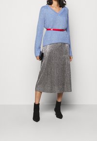 Světle modrý žebrovaný pletený svetr s výstřihem do V, doplněný o metalickou plisovanou midi sukni. Červený pásek zdůrazňuje pas. Černé kotníkové boty.