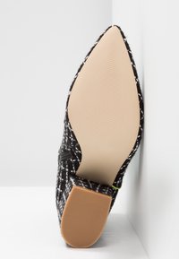 Chaussure texturée noire et blanche à bout pointu avec une semelle beige et un petit talon bloc, affichée droite contre un coin blanc.