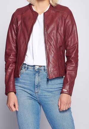 Giacca di pelle borgogna con spalle a coste, chiusura con zip e tasche laterali, abbinata a jeans a vita alta di colore blu chiaro.