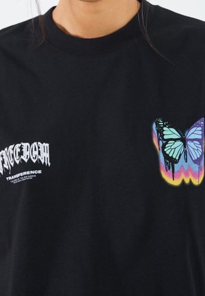 Czarny t-shirt z białym gotyckim napisem „FREEDOM” na lewej piersi oraz kolorowym niebiesko-fioletowym motylem z tęczowym cieniem na prawej piersi.