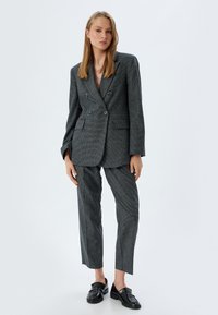 Grijze geruite dubbelgebreide blazer met notch-lapels, twee voorzakken, gecombineerd met bijpassende getailleerde broek en zwarte loafers.