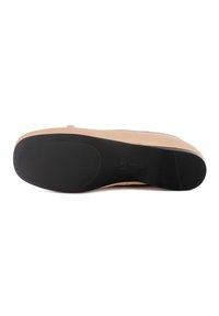 Chaussure en cuir beige à finition lisse, dotée d'une semelle en caoutchouc noire avec motifs de grip texturés et d'un détail de couture discret le long de la tige.