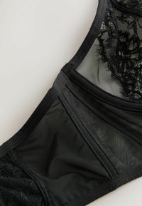 Juodas nėrinių ir tinklelio liemenėlė su sudėtingais gėlių raštais, sklandžiu dirželiu ir struktūrizuota konstrukcija. Savybės: reguliuojamos petnešos ir kabliuko uždarymas.