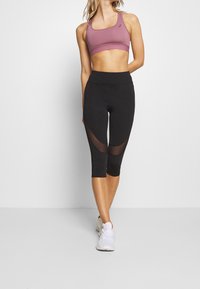 Sorte capri leggings har netpaneler og en høj talje, som er parret med en lavendel sports-bh lavet af strækbart, åndbart stof.