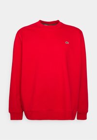 Sweat-shirt en coton rouge avec un col rond, des manches longues, des poignets et un ourlet côtelés. Présente un petit logo vert sur la poitrine.