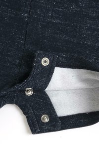 Tissu bleu marine avec un motif texturé et des éclats blancs. Présente des fermetures à pression en métal à l'ouverture, révélant une doublure intérieure douce.