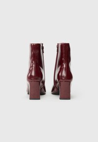 Botine din piele bordo, cu un finisaj neted, tocuri pătrate și fermoare pe lateral. Prezintă un design elegant, cu detalii minime.