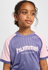 Lila och rosa sporttröja med vertikala ränder, korta ärmar och rund halsringning, med "hummel"-logotypen tydligt synlig.