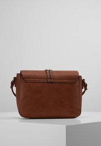 Brązowa skórzana torba na ramię z klapką zapinana na podwójne paski z ozdobnymi ćwiekami. Prostokątny kształt o gładkiej fakturze.