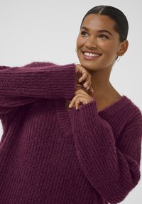 Maglione oversized a V in maglia di un profondo viola con texture a costine. Presenta maniche lunghe e vestibilità comoda.
