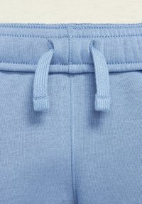 Světle modré teplákové kalhoty s jemnou texturou, elastickým pasem s nastavitelnými stahovacími šňůrkami a pečlivě přišitými švy pro odolnost.