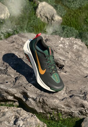 Dark green and black Nike running shoe with orange swoosh, white sole, and red pull tab resting on a large rock outdoors.