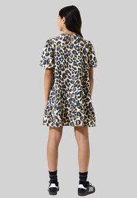 Vestido de estampado de leopardo con mangas cortas abullonadas, detalle de ojal en la parte trasera, dobladillo acampanado y una tela ligera. Combinado con calzado negro y calcetines.