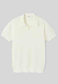 Polo à manches courtes en tricot crème doux et texturé. Présente un col et un ourlet côtelés, avec un détail de logo subtil en bas.