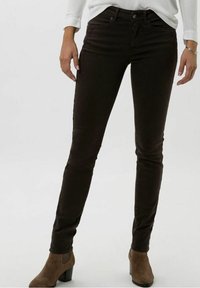 Jeans marrones de corte ajustado con una textura suave, bolsillos frontales y cierre de botón metálico, combinados con botas de tobillo marrones con tacón.