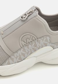 Světle šedé slip-on tenisky s logem MK, síťovinou, detailem na zipu na horní straně a bílou texturovanou podrážkou.