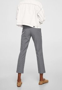 Veste en denim blanche surdimensionnée, pantalons à carreaux noir et blanc, coupe courte, texture douce, associés à des chaussures à enfiler marron clair.
