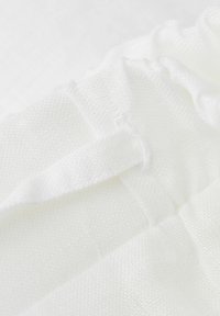 Vit tyg med en texturerad väv, med fållad detaljering och en slät yta. Materialet ser lätt och luftigt ut.