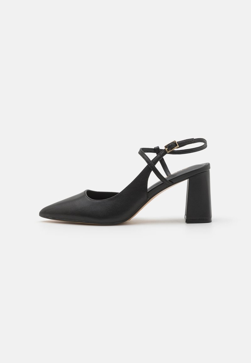 Chaussure slingback en cuir noir avec un bout pointu, une bride à la cheville et un talon carré, présentant une texture lisse et un design minimaliste.