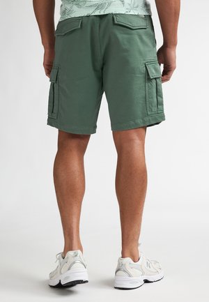 Green cargo shorts made from soft fabric, featuring two side pockets and back pockets. Worn with white sneakers.