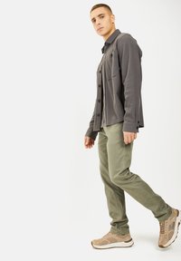 Donkergrijze lange mouwen overhemd met knopen en voorzakken, gecombineerd met olijfgroene broek en tan sneakers, tegen een witte achtergrond.