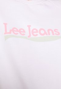 Felpa bianca con il logo "Lee Jeans" in rosa e verde. Presenta una scollatura rotonda e una texture morbida. Design semplice senza dettagli aggiuntivi.