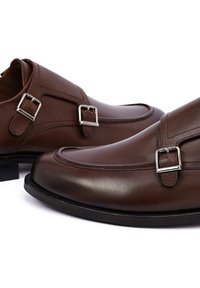 Bruine leren schoenen met een slank ontwerp, voorzien van zilveren gespen en een gladde textuur. Lage hak en ronde neus met gestikte details.