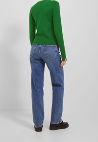 Maglione verde aderente, jeans in denim blu a vita alta, taglio dritto, dettagli sulle tasche posteriori, abbinato a stivali neri grossi.