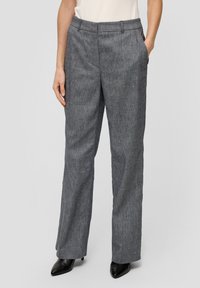 Pantalons gris en mélange de laine avec un design texturé, coupe droite, poches latérales et ceinture ajustée, associés à des chaussures à talons noirs.