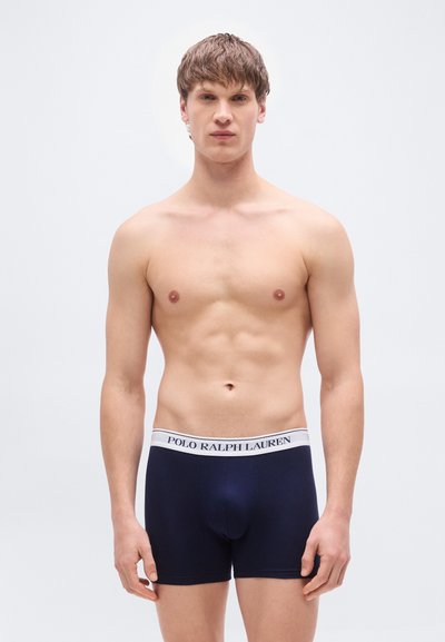 Σκούρα μπλε ανδρικά εσώρουχα τύπου boxer με λευκή ελαστική μέση και λογότυπο. Το ύφασμα φαίνεται λείο και εφαρμοστό, με κλασική γραμμή και χωρίς ορατά σχέδια ή διακοσμητικά.