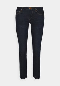 Jeans de mezclilla azul oscuro con corte ajustado, que presentan costuras naranjas, cinco bolsillos y cierre frontal de botón. Corte de pierna recta.