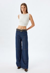Valkoinen teksturoitu crop-top yhdistettynä Rennon tummansinisiin farkkuihin, joissa on näkyvät saumat ja musta vyö metallisoljella.