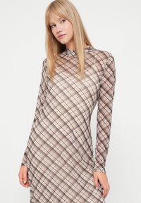 Μακρύ μανίκι φόρεμα σε διαφανές, μοτίβο ύφασμα με καρό σχέδιο σε μπεζ, καφέ και λευκούς τόνους, με υψηλή λαιμόκοψη.