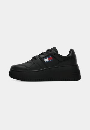 Black sneaker with a textured rubber sole, featuring a padded collar, lace-up front, and a colorful logo patch on the side.