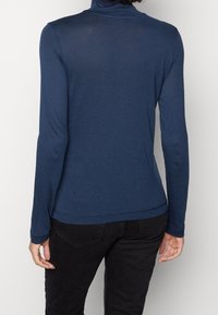 Marinblå långärmad polotröja i lätt stickad tyg med mjuk textur. Har en figurnära silhuett och subtila sömnadsdetaljer.