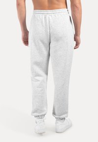 Graue Sweatpants mit einem elastischen Bund, Bündchen an den Knöcheln und einer weichen Textur, kombiniert mit weißen Schuhen. Sichtbare Rückansicht.
