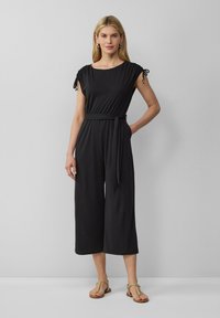 Schwarzer Jumpsuit mit kurzen, gerafften Ärmeln und einem taillierten Bund. Weicher Stoff, weite Beine und runder Halsausschnitt. Minimalistisches Design.