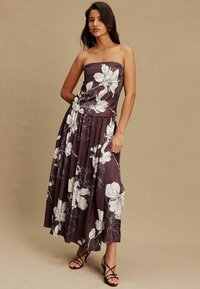 Lila trägerloses Blumenkleid mit weißen Blüten, mittellanger Rock, plissiertes Design, glattes Material, kombiniert mit schwarzen Riemchenschuhen.