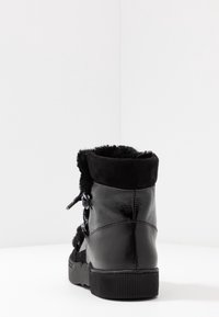 Mustat nilkkurit, joissa on teksturoidut nahkapinnat, mokkasiiniyksityiskohtia ja karvavuorattu kaulus. Ominaisuuksiin kuuluu paksu kumipohja, joka tarjoaa hyvän pidon.