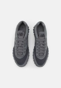 Les baskets grises présentent une combinaison de mesh texturé et de matériaux synthétiques lisses, avec une semelle robuste et un marquage subtil sur la languette.