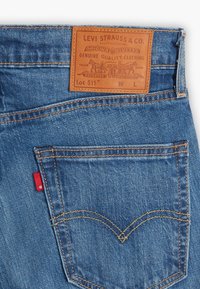 Blue denim jeans back pocket with orange stitching, red Levi’s tag, and leather Levi Strauss & Co. brand patch above the pocket.