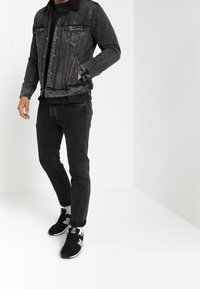 Svart denimjacka med framfickor och fårskinnskrage, kombinerad med svarta jeans och svarta sportskor med vita accenter.