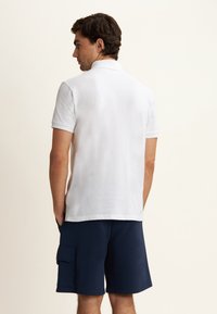 Polo shirt bianco con colletto classico, maniche corte e texture liscia, abbinato a pantaloni cargo blu navy con tasche laterali.