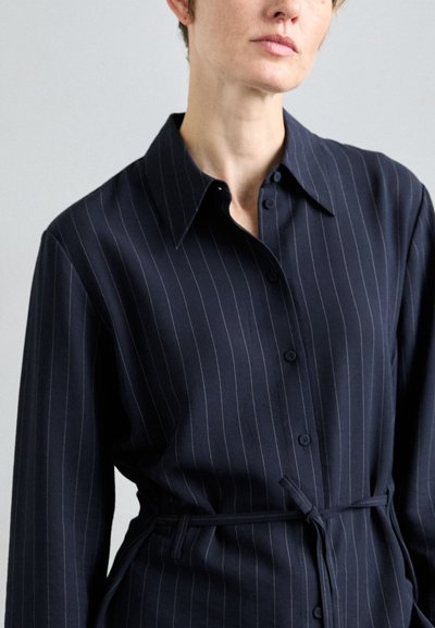 Marineblauwe button-up shirt met verticale witte strepen, lange mouwen, een klassieke kraag en een strik taille detail. Gladde textuur.