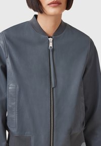 Giacca bomber in pelle blu scuro con zip frontale, colletto a costine e tasche laterali. Texture liscia e dettagli di design sobrii.