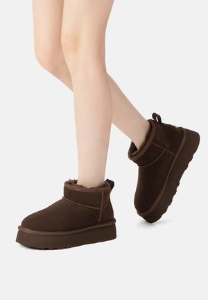 Brown suede ankle boots with a round toe, shearling lining, and a thick platform sole. Mid-height design with a soft, textured finish.