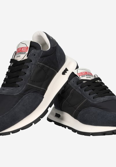 Schwarze und graue Sneaker aus einer Kombination von Wildleder und Nylonmaterialien, mit Schnürsenkeln und kontrastierenden weißen Sohle.